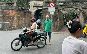 Scooter and pedestrian near ancient gate in Hanoi Old Quarter.