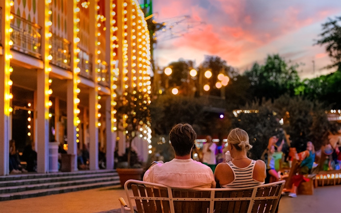 Couple sitting on a bench at Tivoli Gardens, Copenhagen during evening lights.