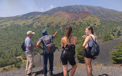 Group of tourists with guide on Mount Etna, Catania, pointing at volcanic landscape.