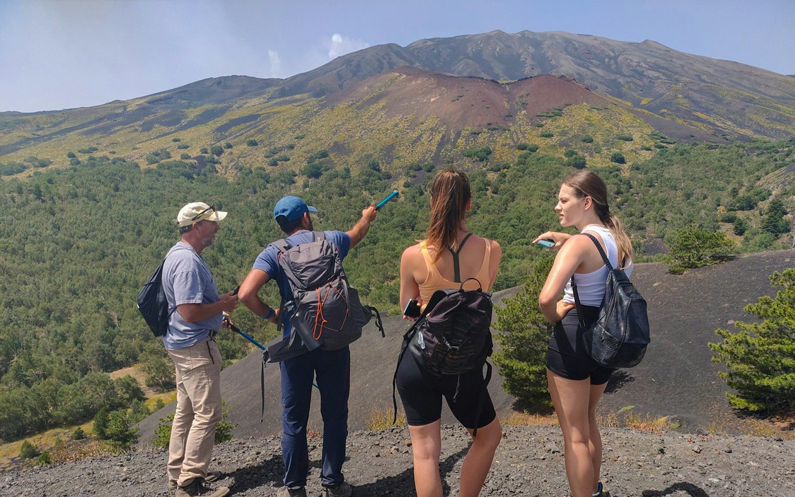 Group of tourists with guide on Mount Etna, Catania, pointing at volcanic landscape.