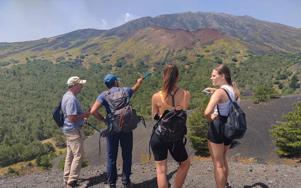 Group of tourists with guide on Mount Etna, Catania, pointing at volcanic landscape.
