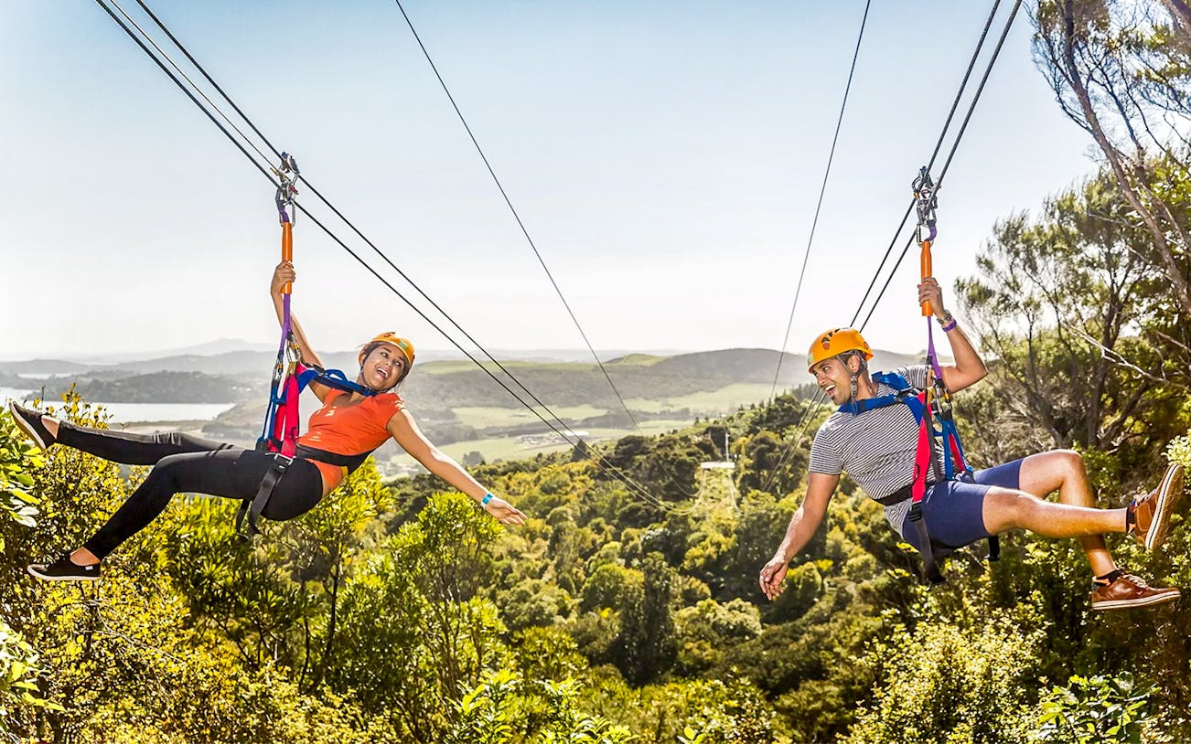 Couple ziplining over forest on Waiheke Island, New Zealand.