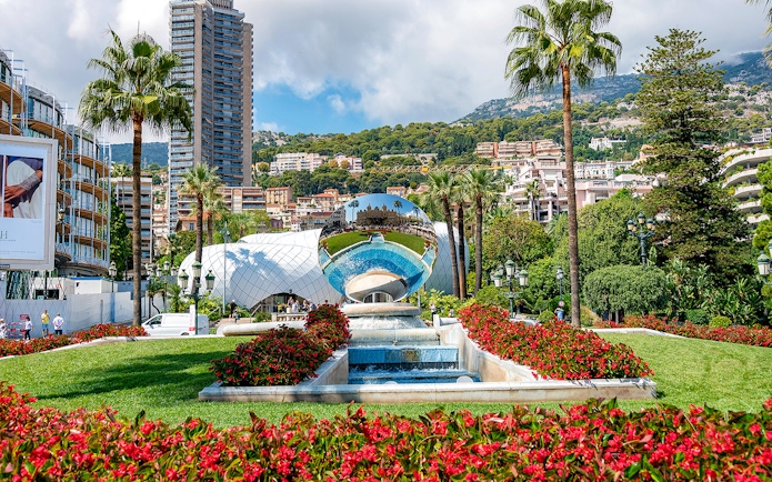 Monaco Casino Gardens with reflective sculpture and palm trees.