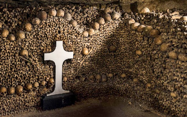 Catacombs entrance with skulls and bones arranged around a white cross.