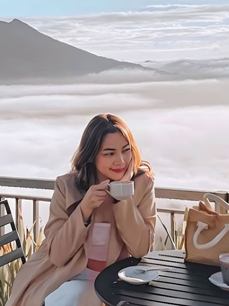 Woman enjoying coffee with a view of Mount Batur during Kintamani sunrise tour.
