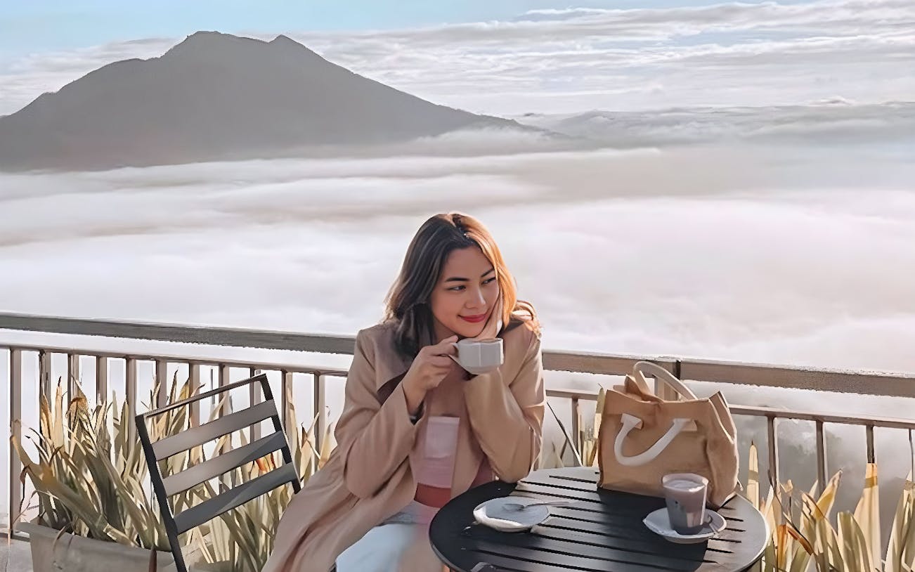 Woman enjoying coffee with a view of Mount Batur during Kintamani sunrise tour.