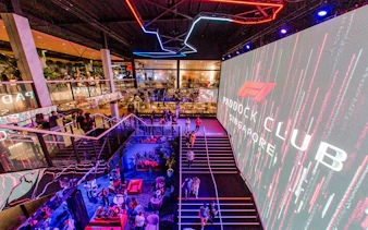 Paddock Club Singapore interior with guests and large digital display.
