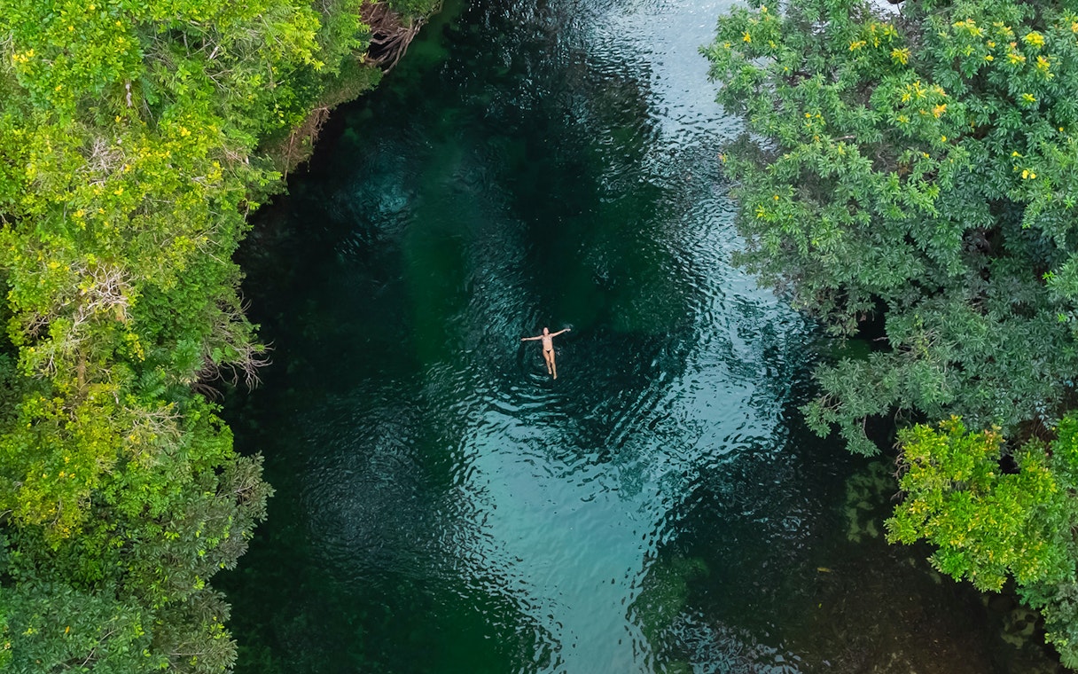 Person floating in a river surrounded by lush greenery in Queensland.