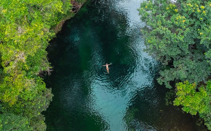 Person floating in a river surrounded by lush greenery in Queensland.