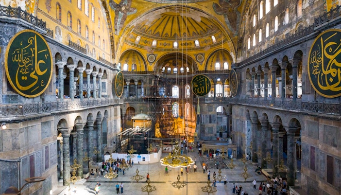 Interior of Hagia Sophia with visitors, showcasing ornate arches and large calligraphic medallions, Istanbul.