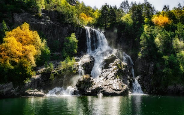 Waterfall cascading over rocks in Lysefjord, Norway, surrounded by lush green and autumn trees.