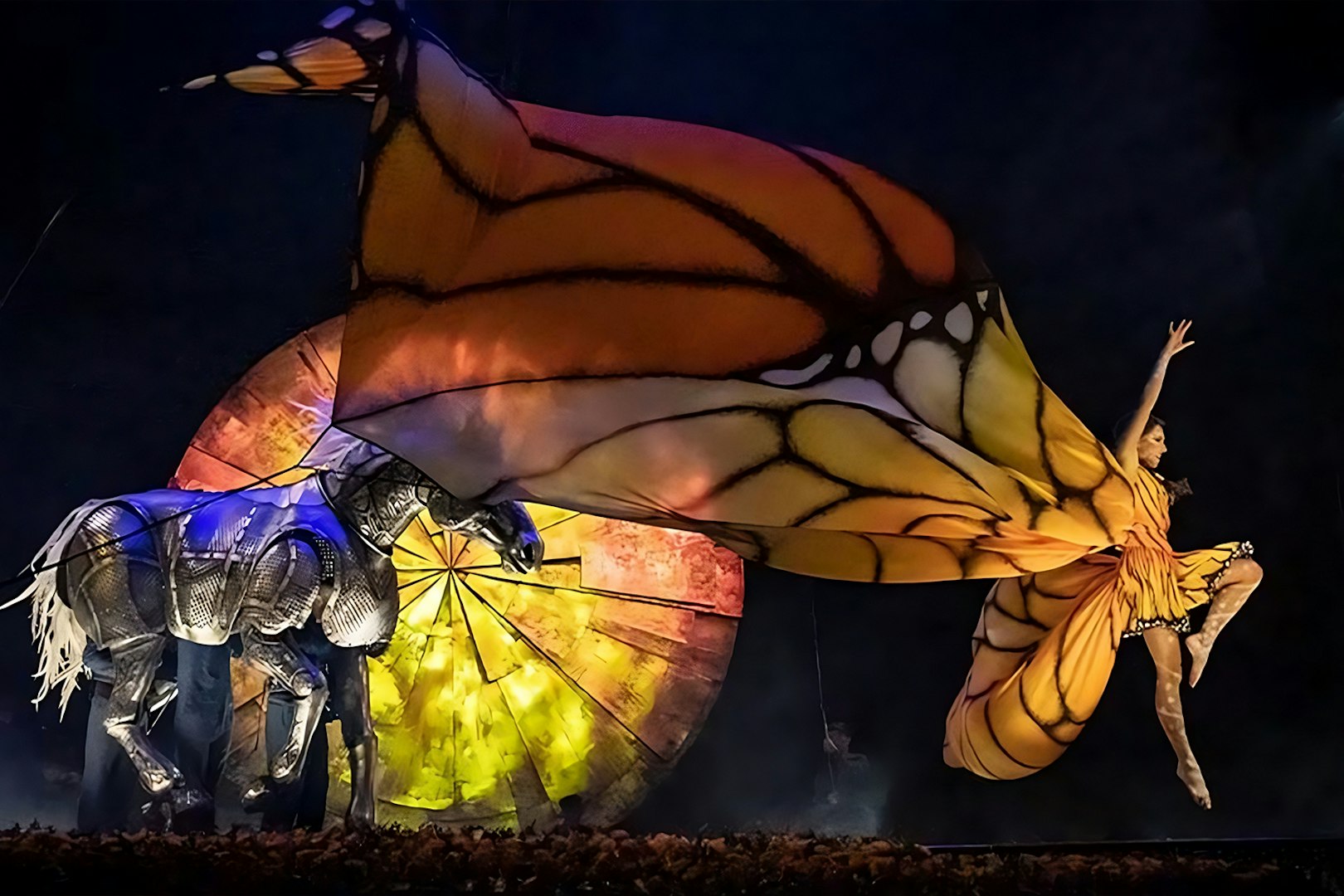 Performer in butterfly costume leaping beside mechanical horse in Luzia show.