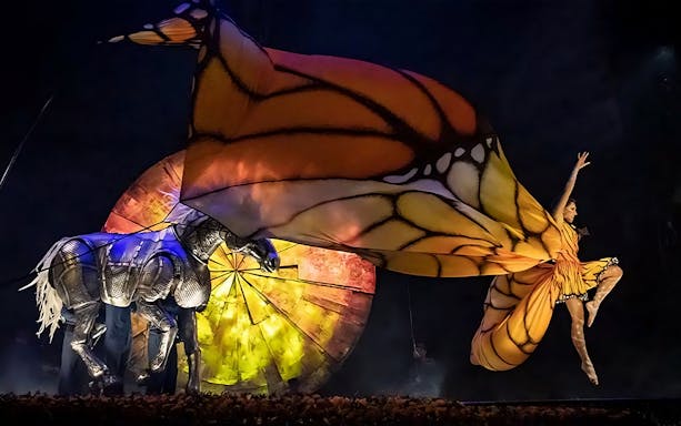 Performer in butterfly costume leaping beside mechanical horse in Luzia show.