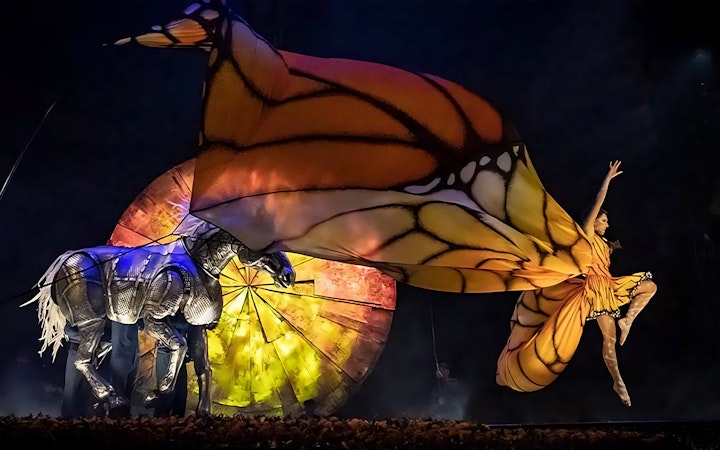 Performer in butterfly costume leaping beside mechanical horse in Luzia show.