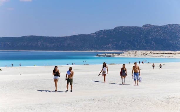 Tourists walking on the white travertines of Pamukkale with turquoise water and mountains in the background, Antalya.
