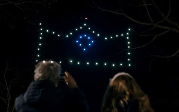 Camp Nou drone show forming a crown shape in the night sky, viewed by spectators.