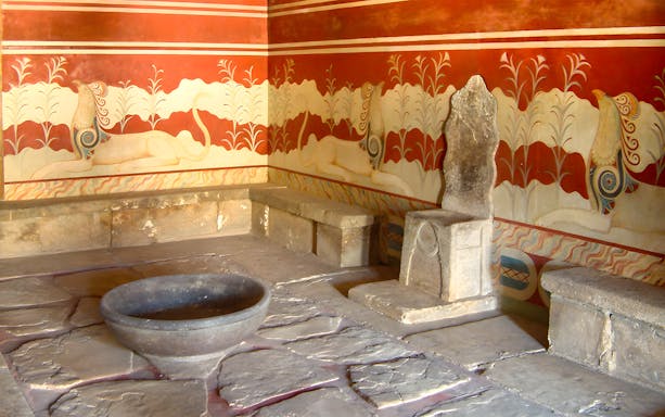 Throne room at Knossos Palace with stone seat and frescoes.