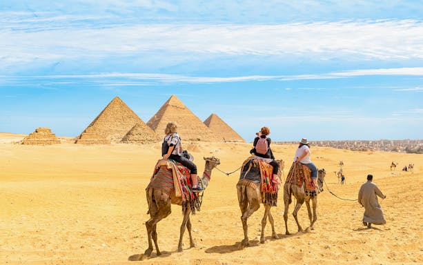 Tourists on camels approaching the Giza Pyramids in Egypt.