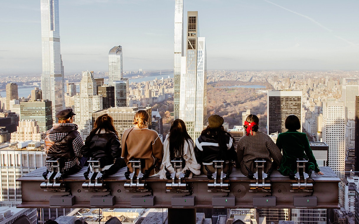 Visitors seated on a rooftop edge overlooking New York City skyline at Rockefeller Center.