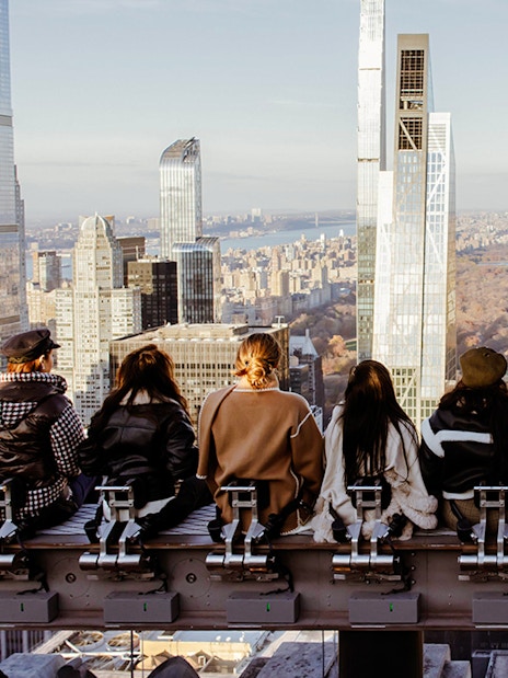 Visitors seated on a rooftop edge overlooking New York City skyline at Rockefeller Center.