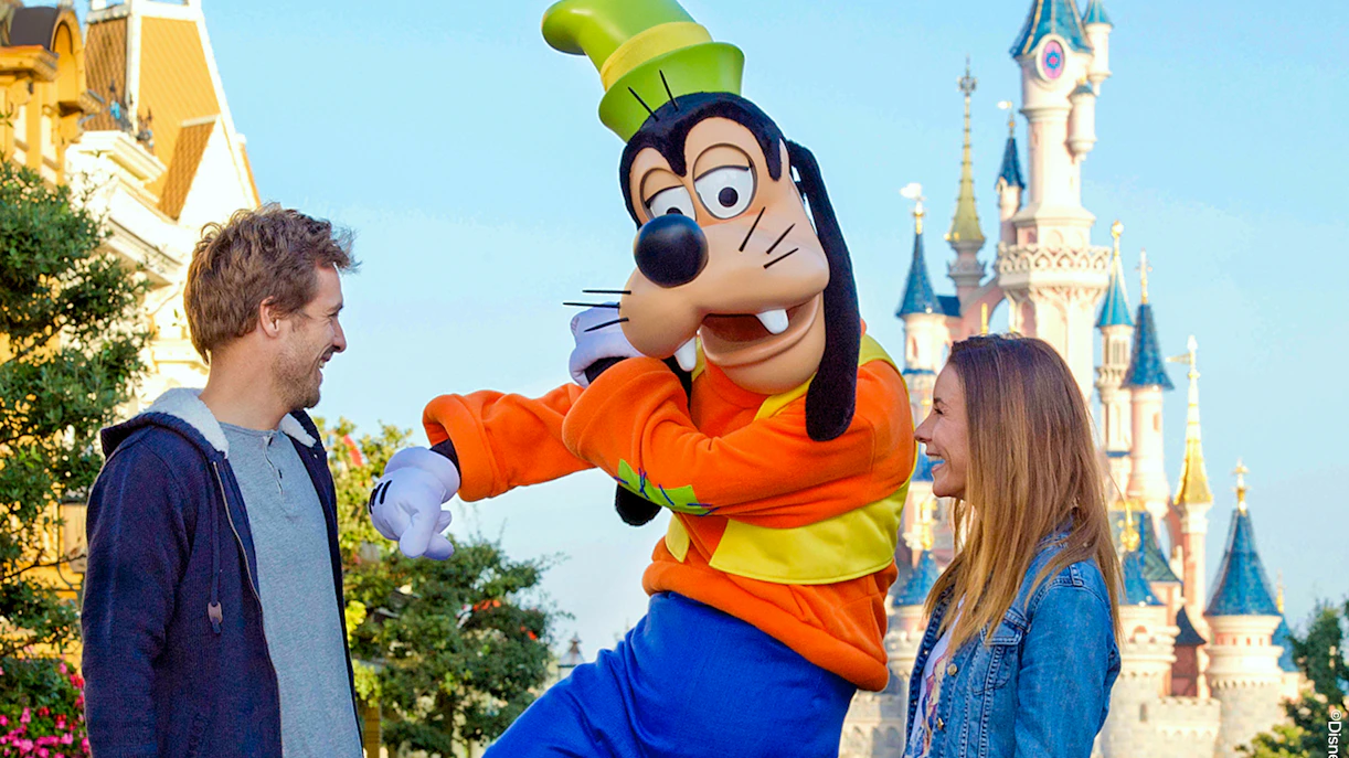 Goofy character meeting visitors at Disneyland Paris with Sleeping Beauty Castle in background.