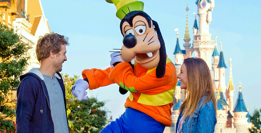 Goofy character meeting visitors at Disneyland Paris with Sleeping Beauty Castle in background.