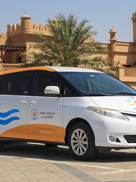 Tour vehicle parked in front of traditional Arabian architecture for Arabian Dunes Premium Safari.
