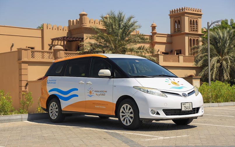 Tour vehicle parked in front of traditional Arabian architecture for Arabian Dunes Premium Safari.