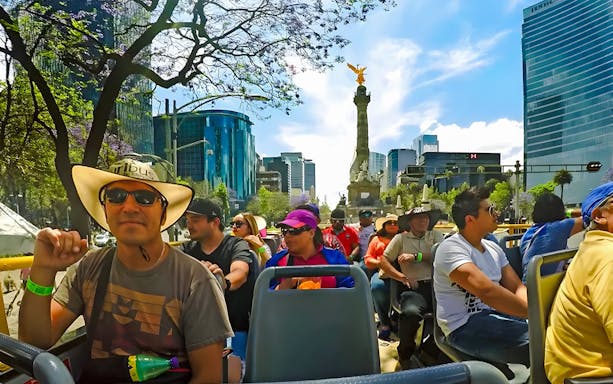 Tourists on an open-top bus near the Angel of Independence in Mexico City's historic center.