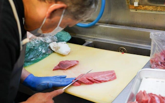 Person slicing tuna at Tsukiji Market during Tokyo tour.