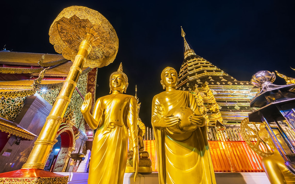 Golden Buddha statues at Wat Phra That Doi Suthep, Chiang Mai, with temple spire in background.