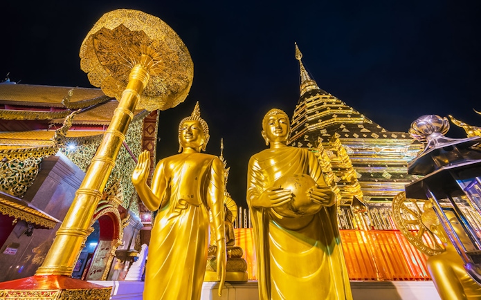 Golden Buddha statues at Wat Phra That Doi Suthep, Chiang Mai, with temple spire in background.