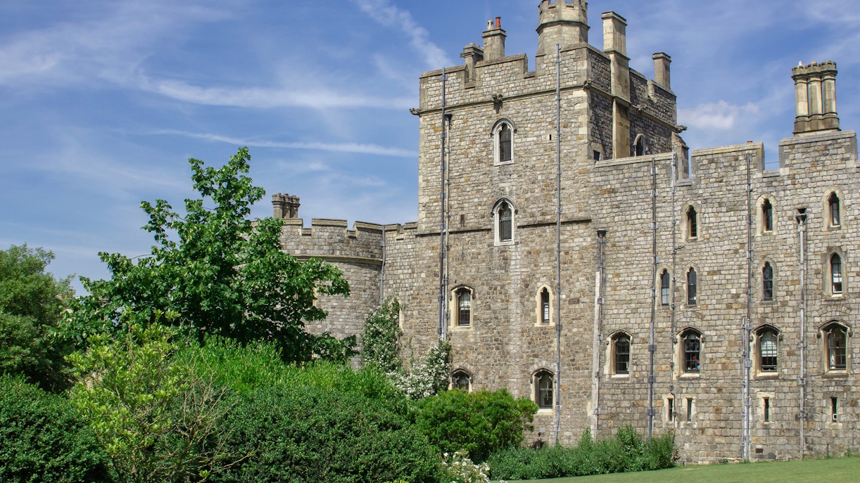 Windsor Castle stone exterior with lush greenery and blue sky.