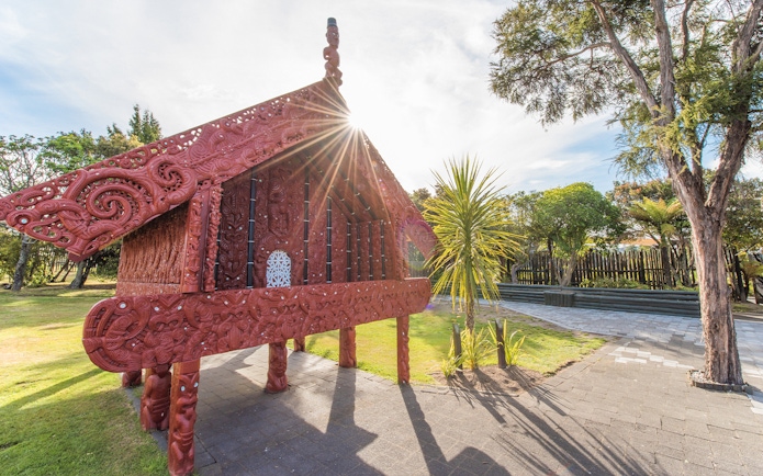 Traditional Māori carving at Te Puia, Rotorua, New Zealand, with sunlight streaming through.