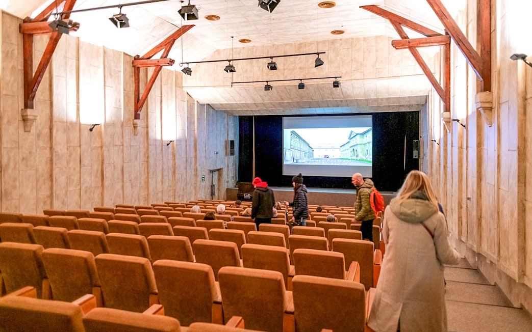 Guests inside Terezin Concentration Camp theater, viewing historical presentation.