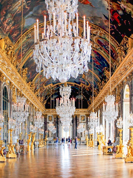 Hall of Mirrors in Versailles Palace with chandeliers and ornate decor.