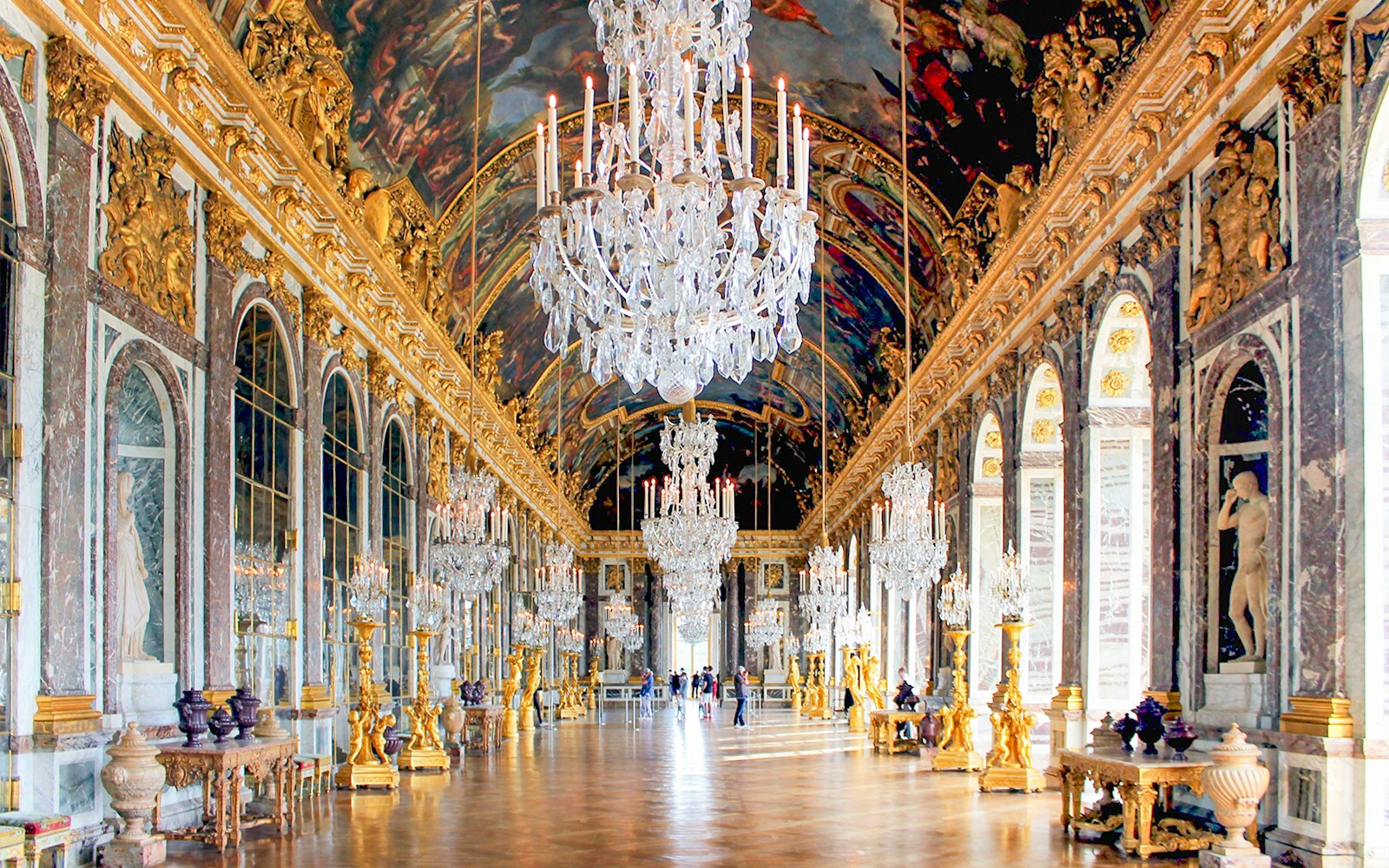Hall of Mirrors in Versailles Palace with chandeliers and ornate decor.