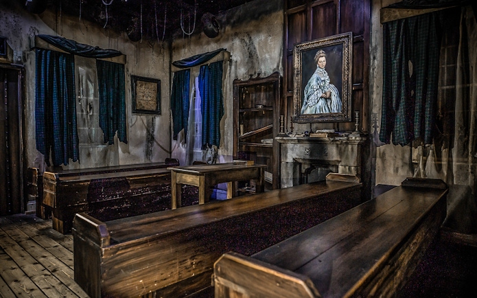 Edinburgh Dungeon room with wooden benches and a portrait, part of Castle Ghosts tour.
