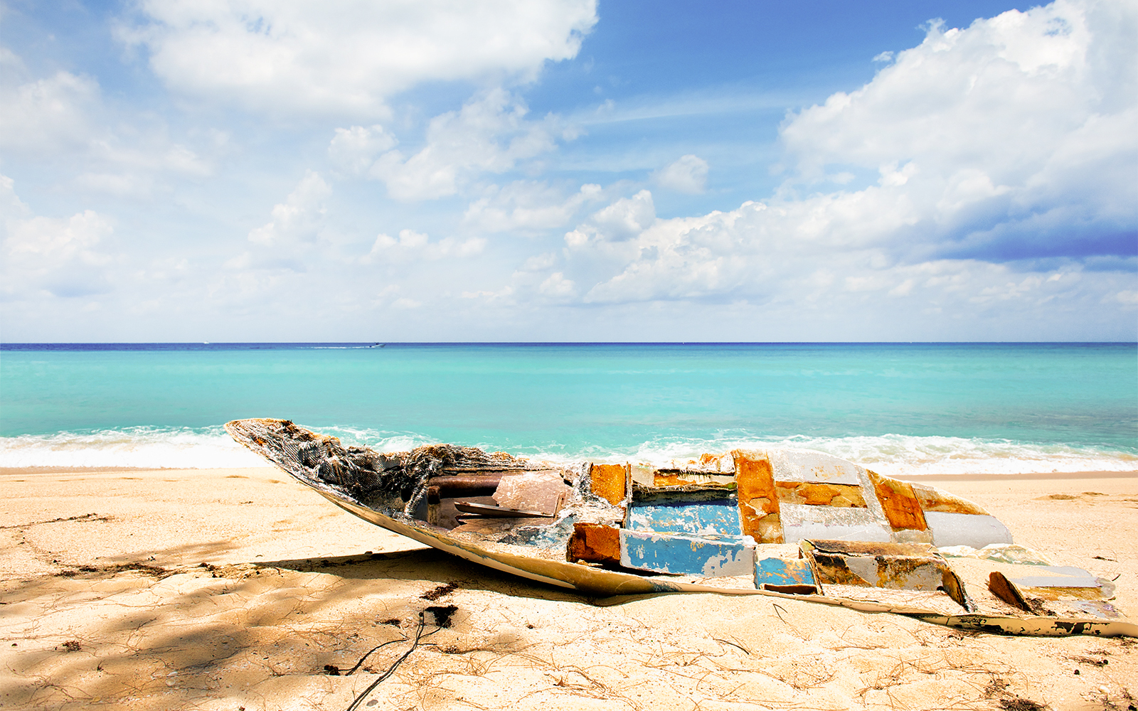 Abandoned boat on a sandy beach with turquoise water in Bimini, Bahamas.
