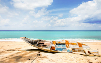 Abandoned boat on a sandy beach with turquoise water in Bimini, Bahamas.