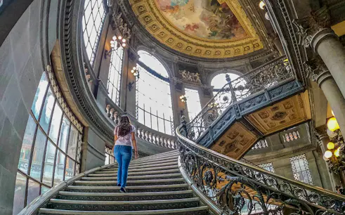 Grand staircase inside a historical building in Mexico City, featuring ornate railings and a painted ceiling.