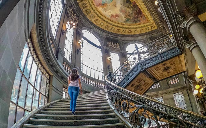 Grand staircase inside a historical building in Mexico City, featuring ornate railings and a painted ceiling.