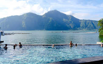 People enjoying a hot spring pool with a view of mountains and a lake in Indonesia.