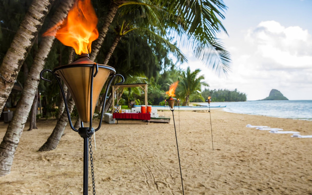 Tiki torches on Secret Island Beach, Kualoa Ranch, Hawaii with palm trees and ocean view.