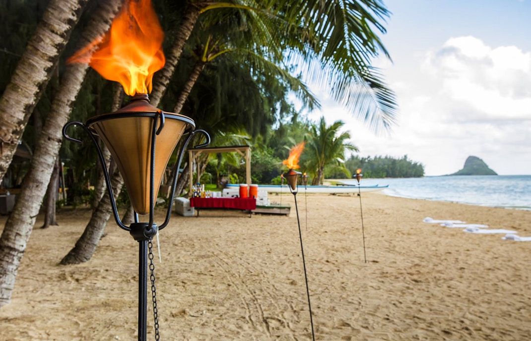 Tiki torches on Secret Island Beach, Kualoa Ranch, Hawaii with palm trees and ocean view.