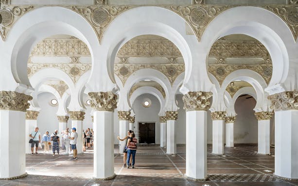 Visitors exploring the arches inside Synagogue of Santa María la Blanca, Toledo.