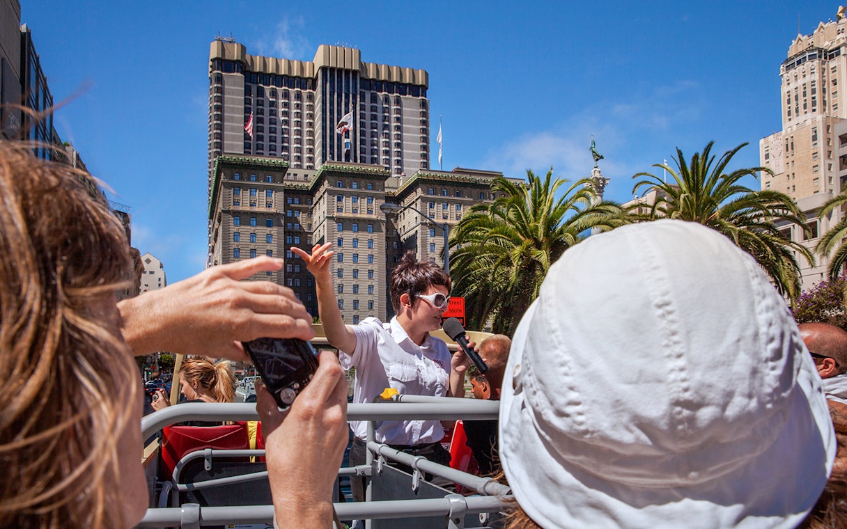 Tour guide speaking on a Big Bus in San Francisco with city buildings in the background.