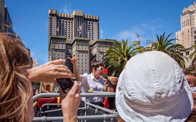 Tour guide speaking on a Big Bus in San Francisco with city buildings in the background.