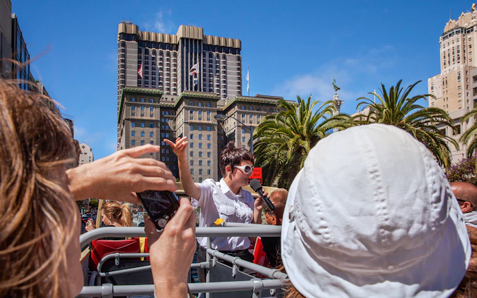 Tour guide speaking on a Big Bus in San Francisco with city buildings in the background.