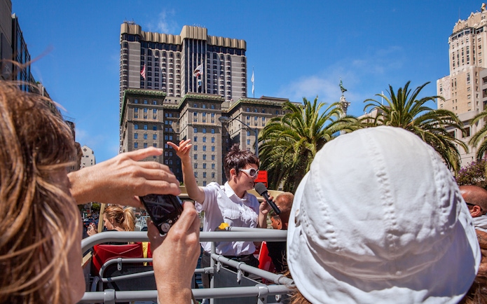 Tour guide speaking on a Big Bus in San Francisco with city buildings in the background.